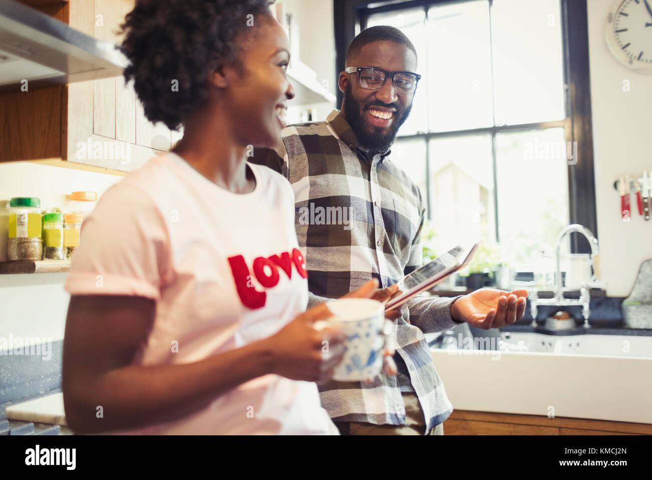 Young couple drinking coffee and using digital tablet in kitchen Stock Photo