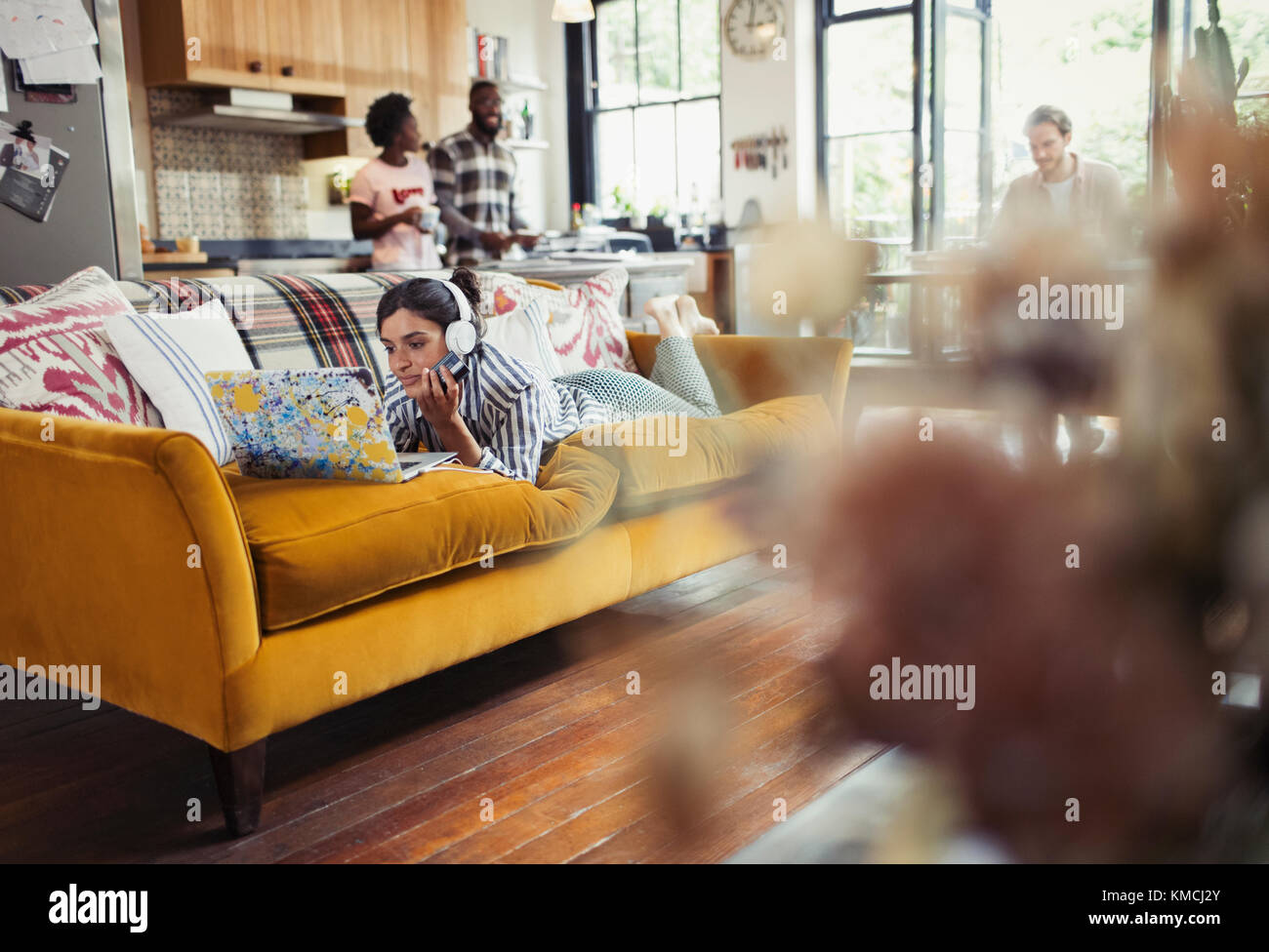 Young woman with headphones using laptop on living room sofa Stock Photo