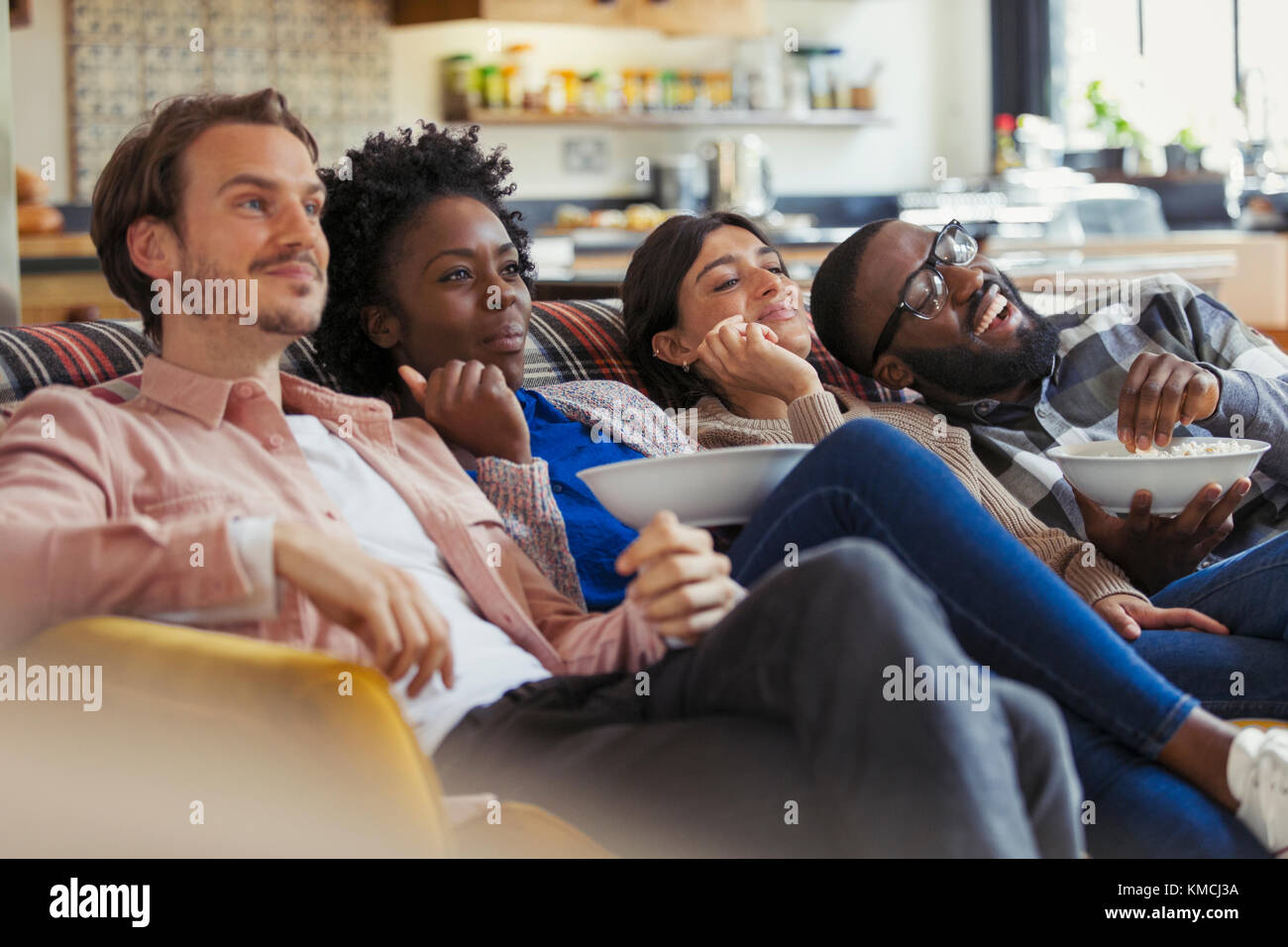 Couples watching TV and eating popcorn on living room sofa Stock Photo