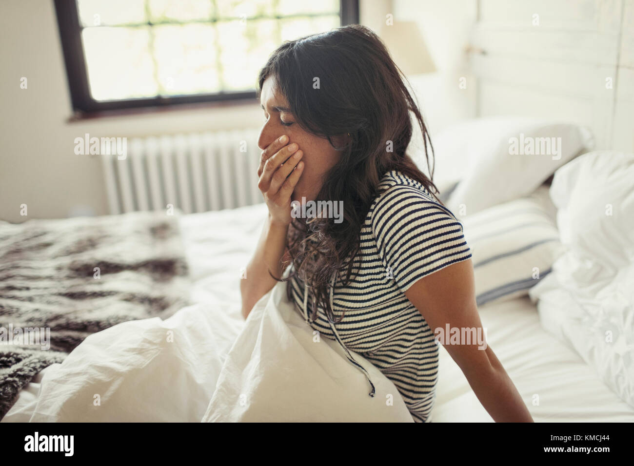 Tired young woman yawning in bed Stock Photo