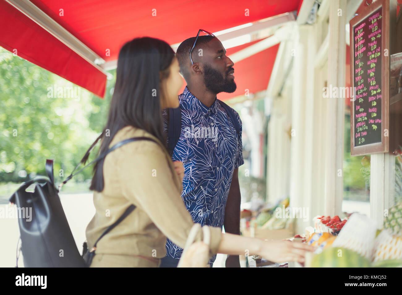 Young couple shopping for produce, looking at prices at outdoor market Stock Photo