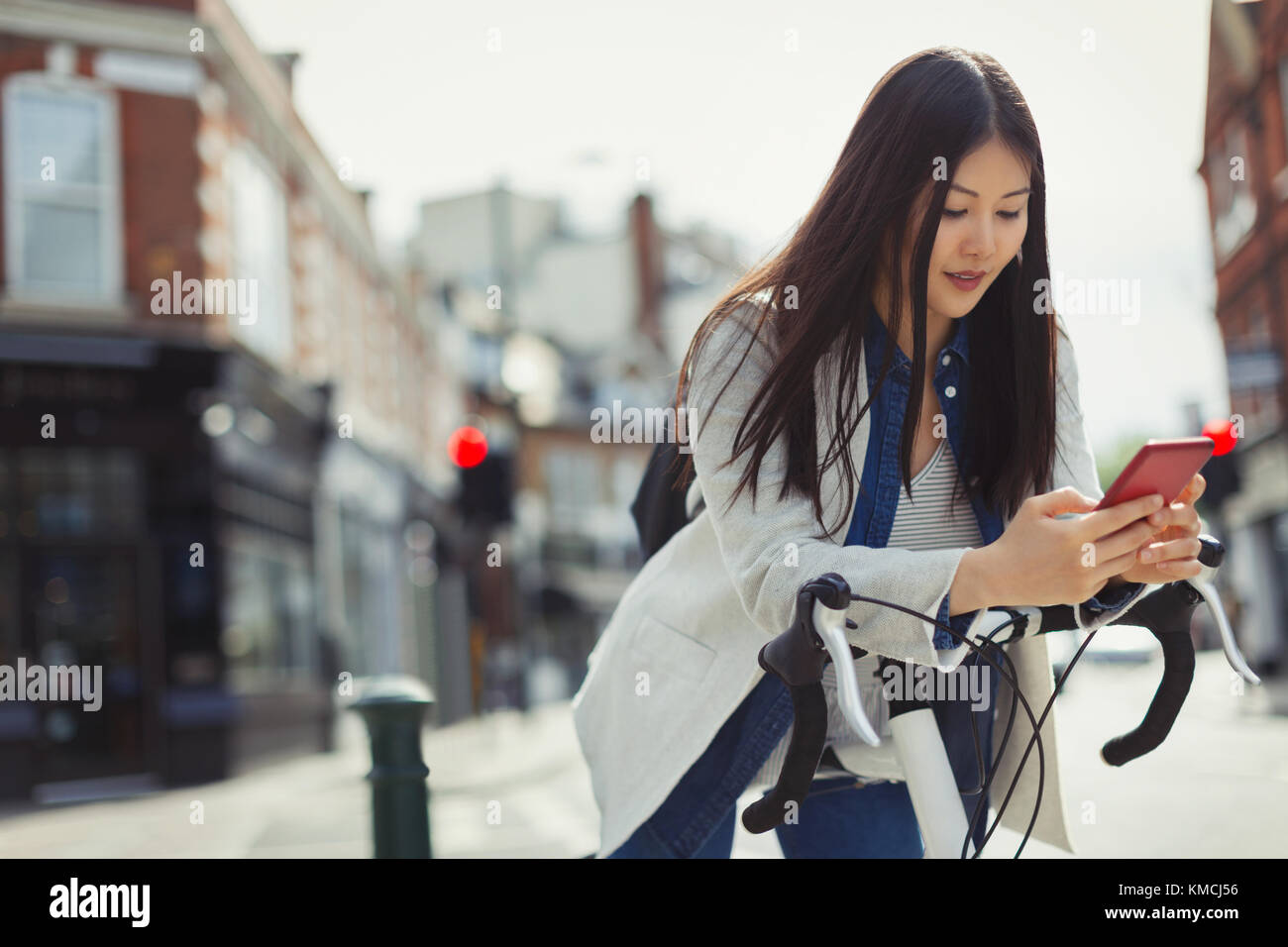 Young woman commuting on bicycle, texting with cell phone on sunny urban street Stock Photo