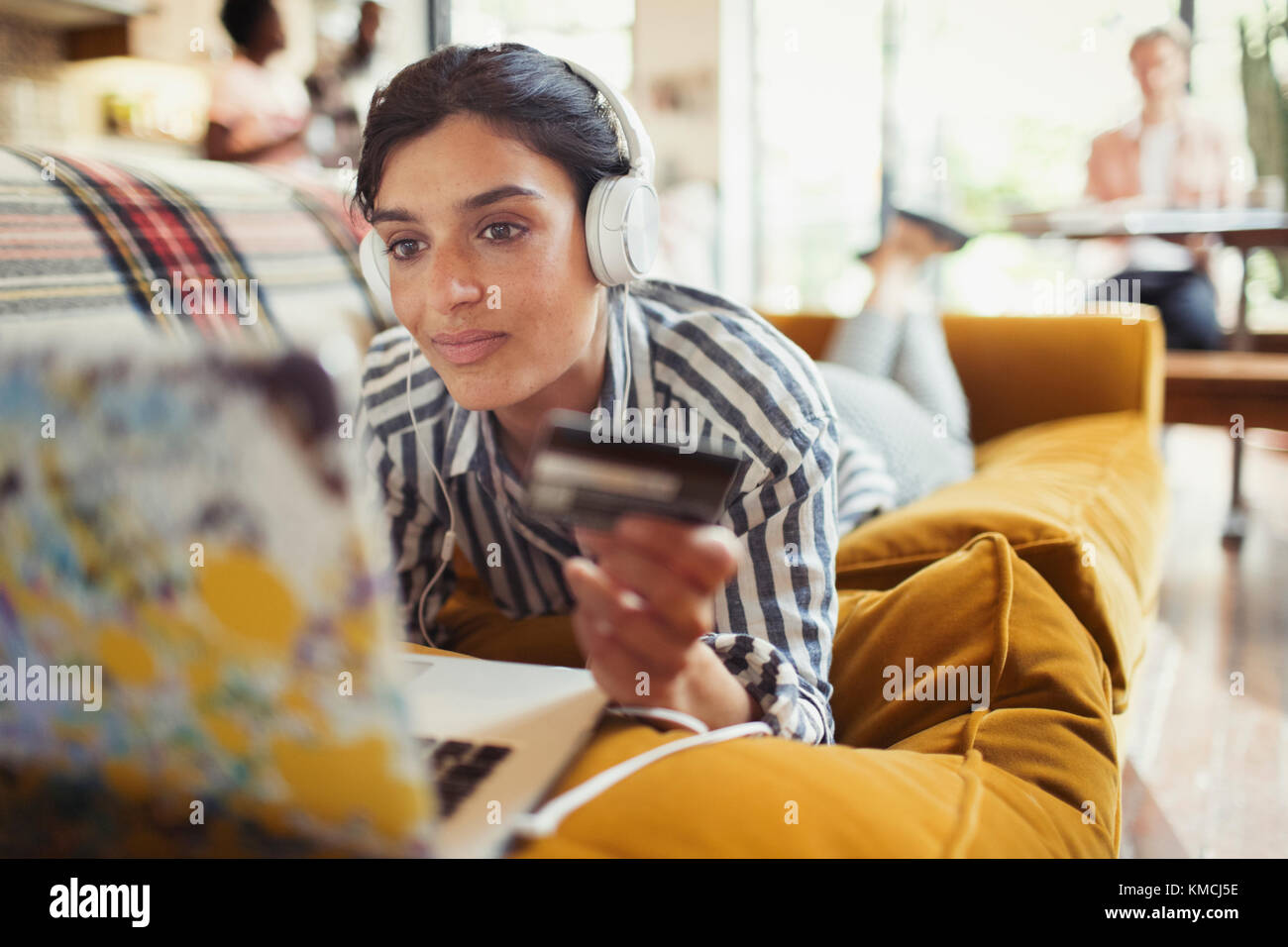 Young woman with credit card and headphones online shopping at laptop on living room sofa Stock Photo