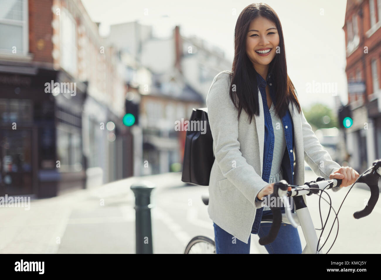 Portrait smiling businesswoman commuting on bicycle on sunny urban street Stock Photo