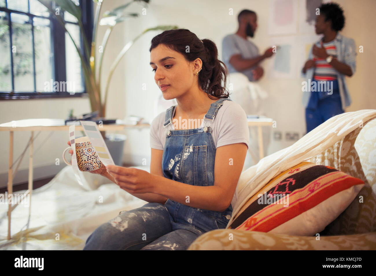 Young woman drinking coffee and viewing paint swatches in living room Stock Photo