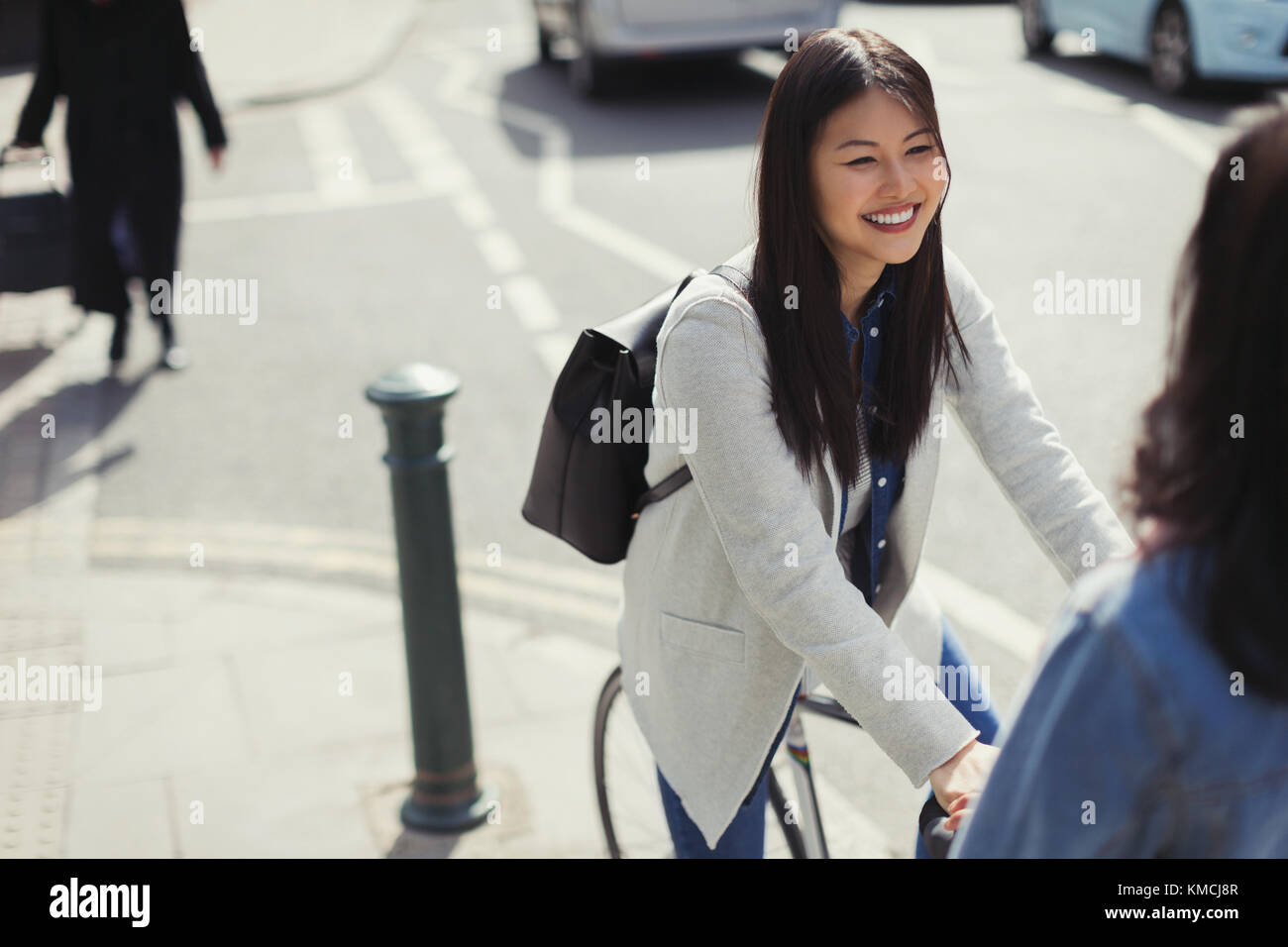 Smiling young woman commuting, riding bicycle on sunny urban sidewalk Stock Photo