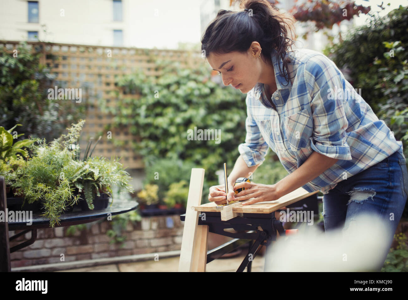 Young woman measuring and marking wood on patio Stock Photo