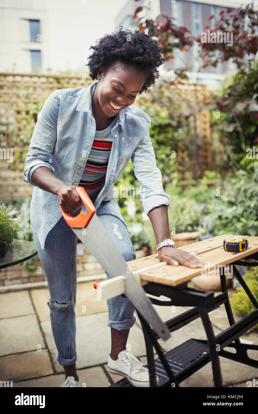 Smiling woman with saw cutting wood on patio Stock Photo