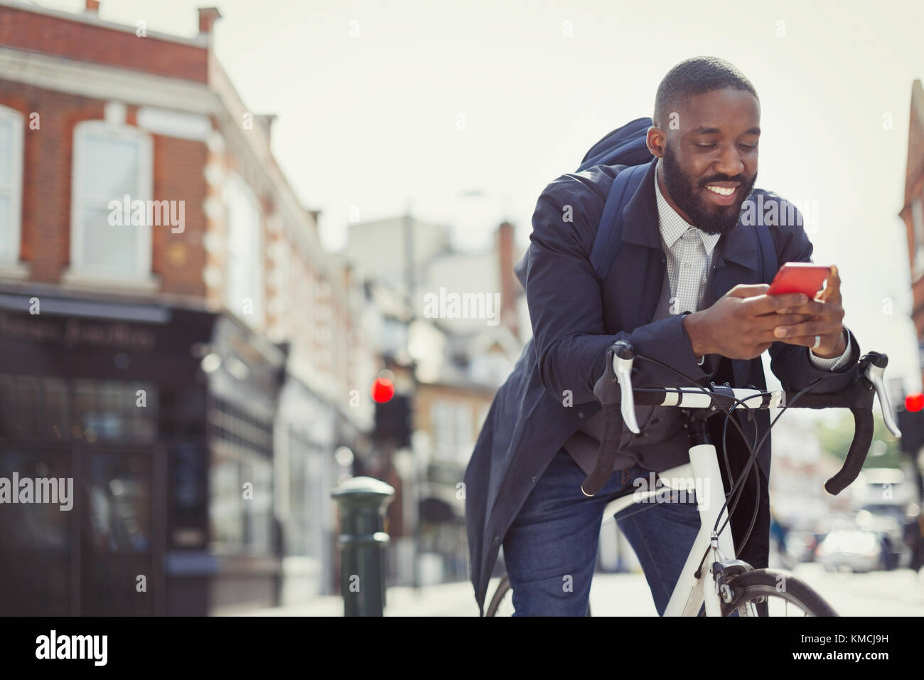 Young businessman commuting with bicycle, texting with cell phone on sunny urban street Stock Photo