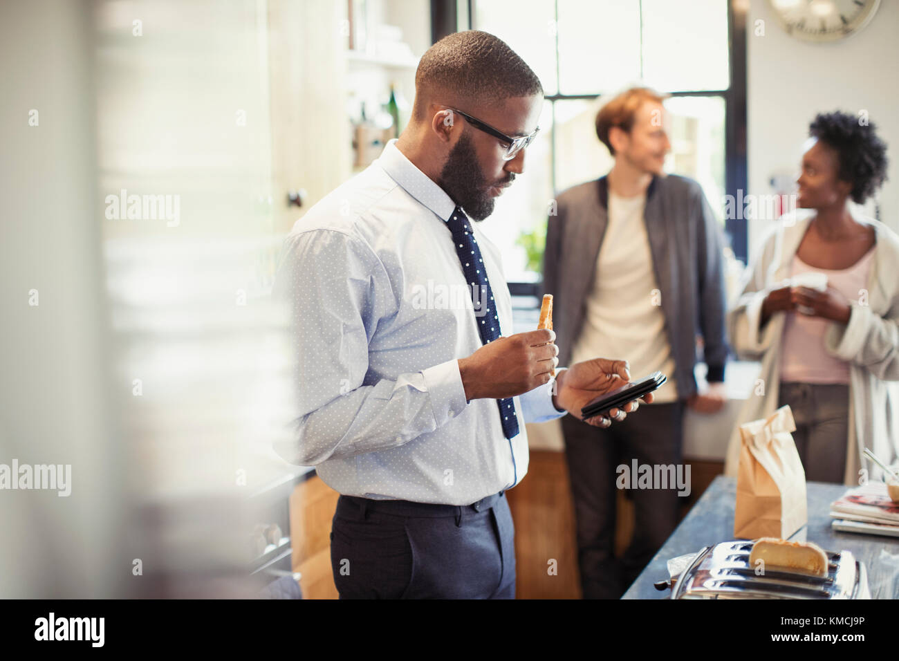 Businessman eating breakfast and texting with smart phone in kitchen ...