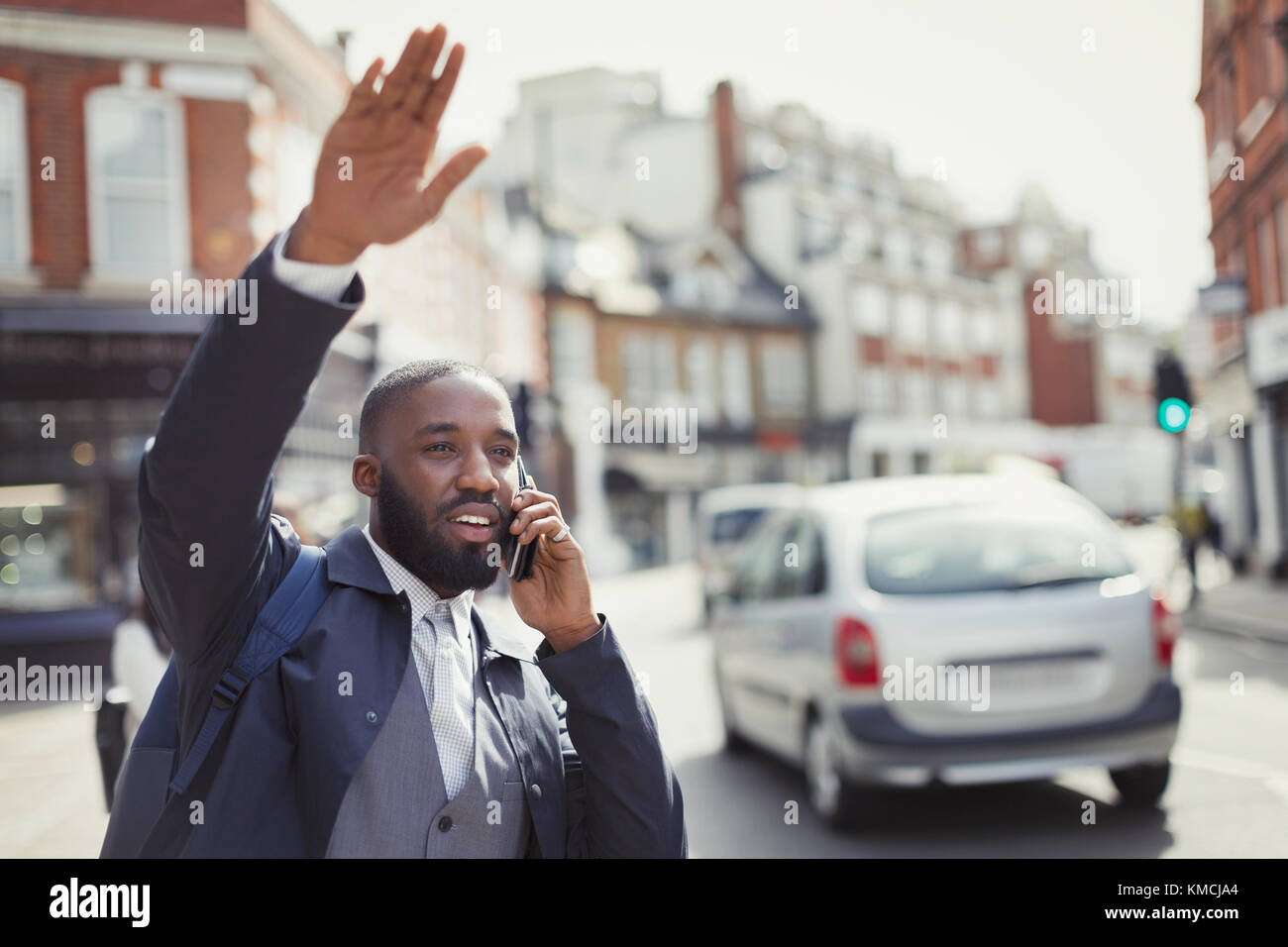 Young businessman talking on cell phone and hailing taxi on sunny urban street Stock Photo