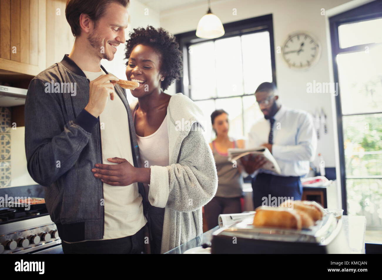 Boyfriend feeding toast to girlfriend in kitchen Stock Photo