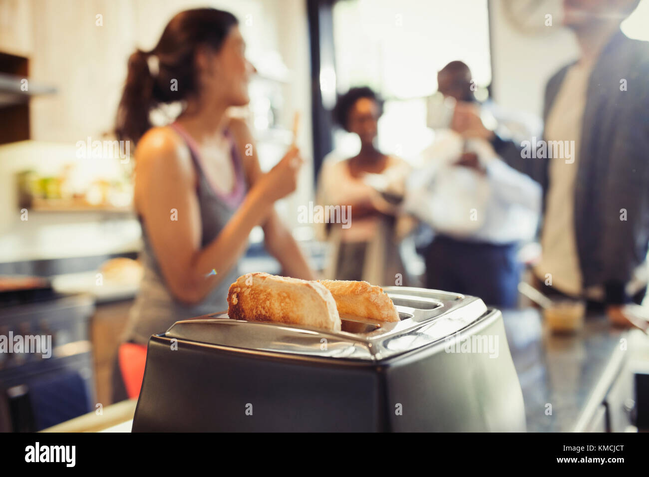 Friend roommates talking behind toast in toaster in kitchen Stock Photo