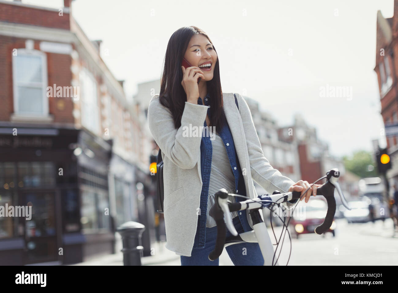 Smiling young woman commuting on bicycle, talking on cell phone on sunny urban street Stock Photo