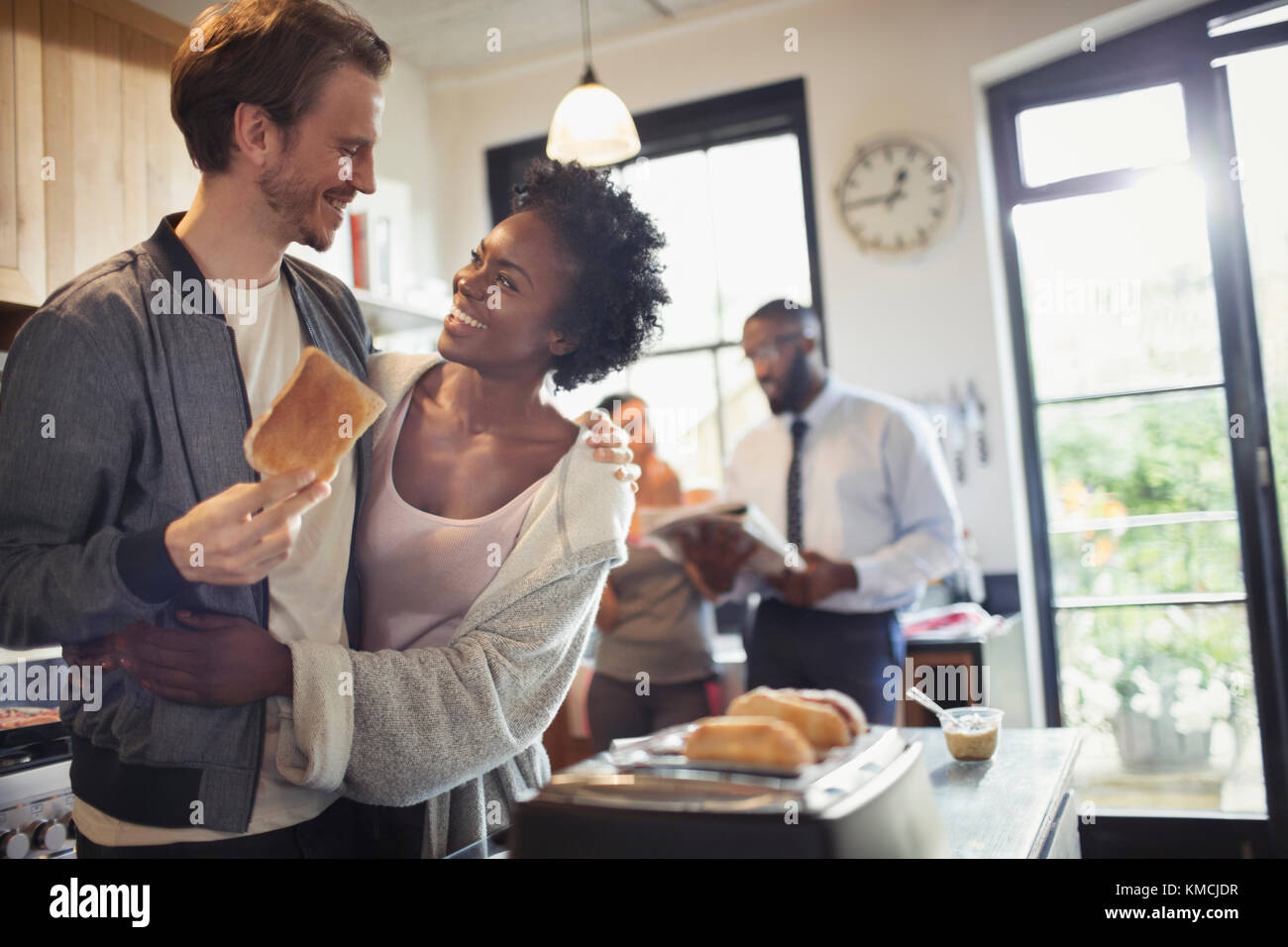 Affectionate couple hugging and eating toast in morning kitchen Stock Photo