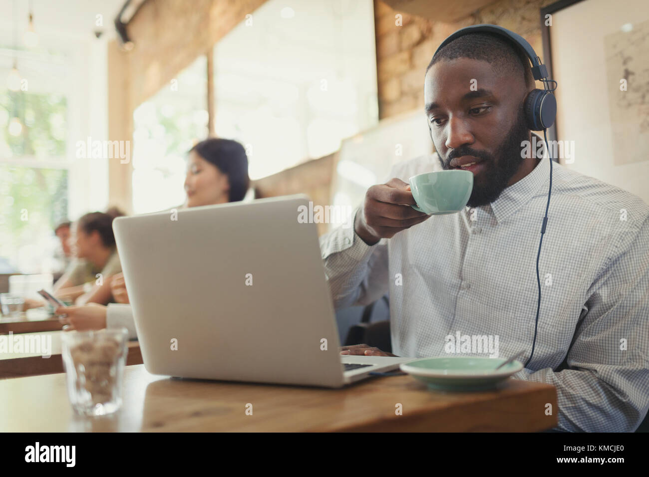 Man with headphones using laptop and drinking coffee in cafe Stock Photo