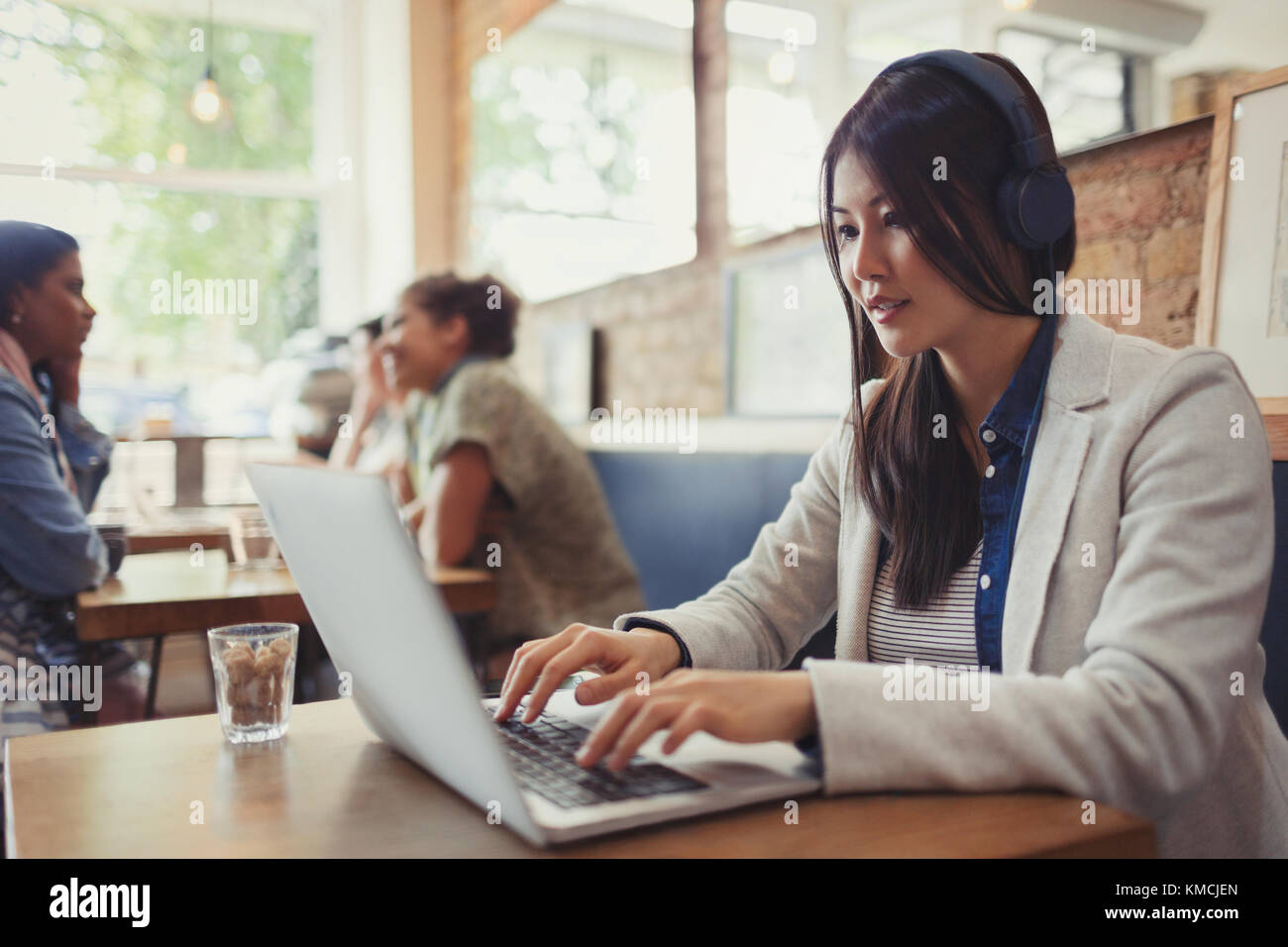 Young woman with headphones using laptop at cafe table Stock Photo