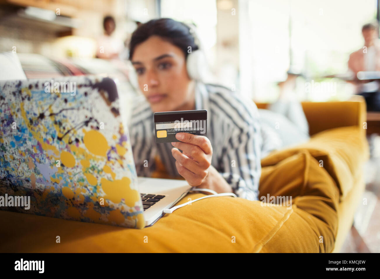 Young woman with headphones and credit card online shopping at laptop on living room sofa Stock Photo