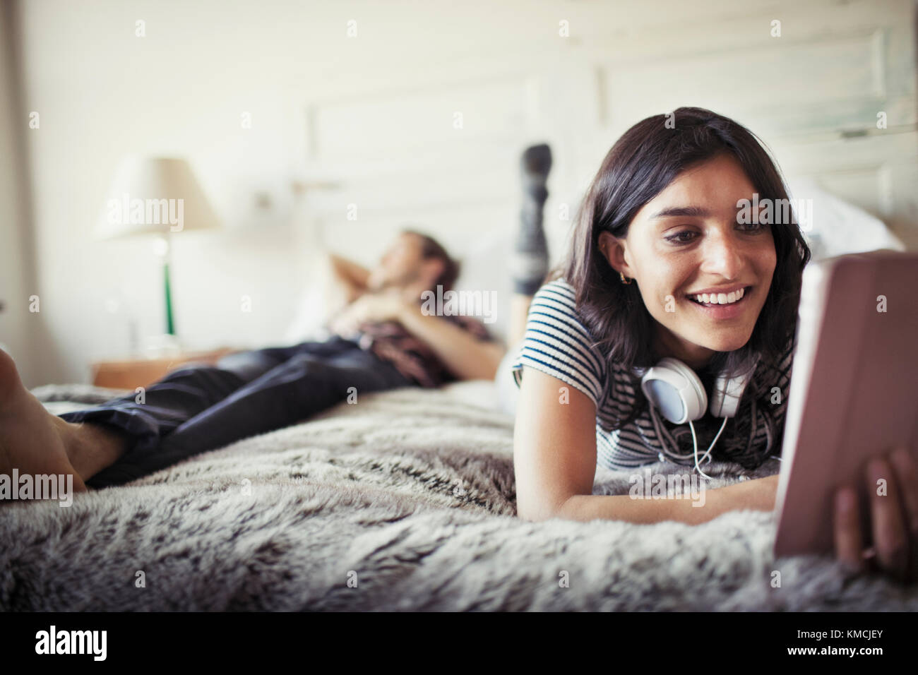 Smiling young woman with headphones using digital tablet on bed Stock Photo