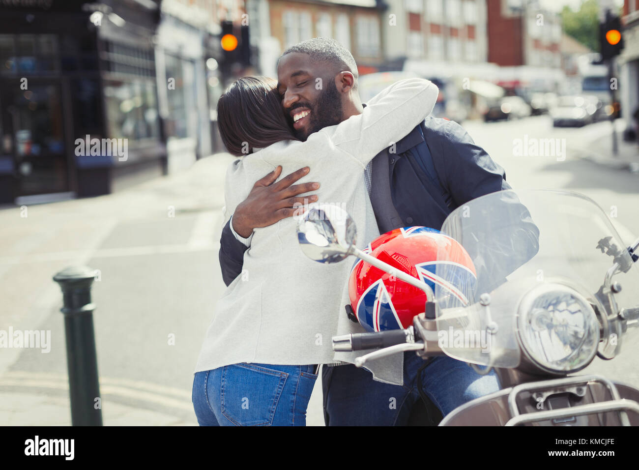 Affectionate young couple hugging at motor scooter on sunny urban street Stock Photo
