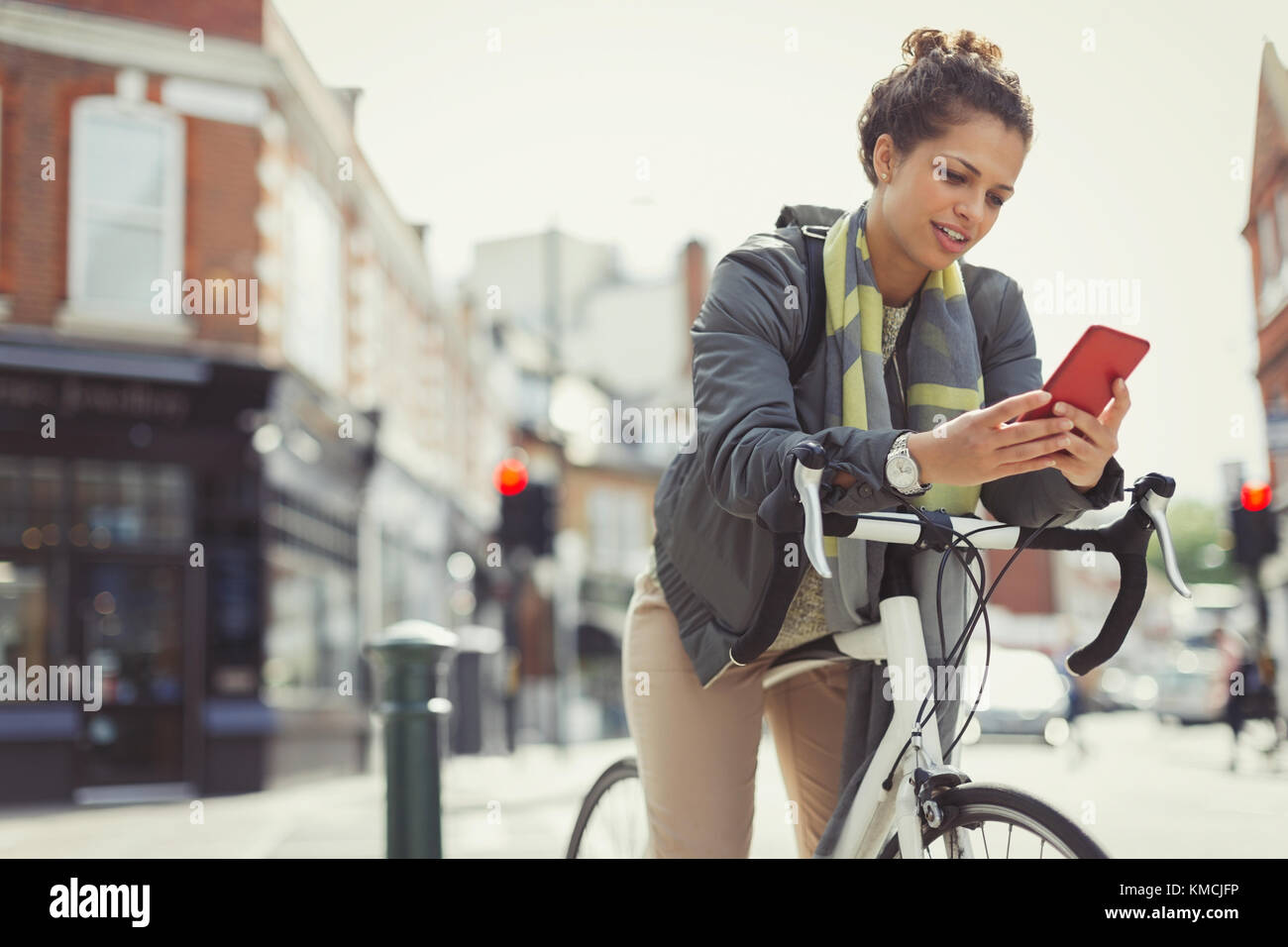 Young woman texting with cell phone, commuting on bicycle on urban street Stock Photo
