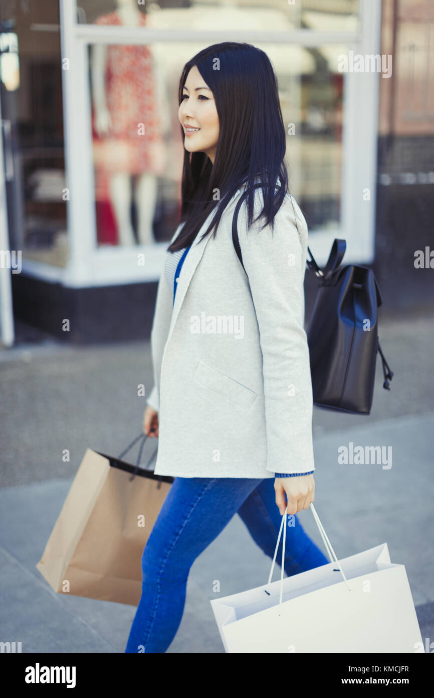 Young woman walking along storefront with shopping bags Stock Photo