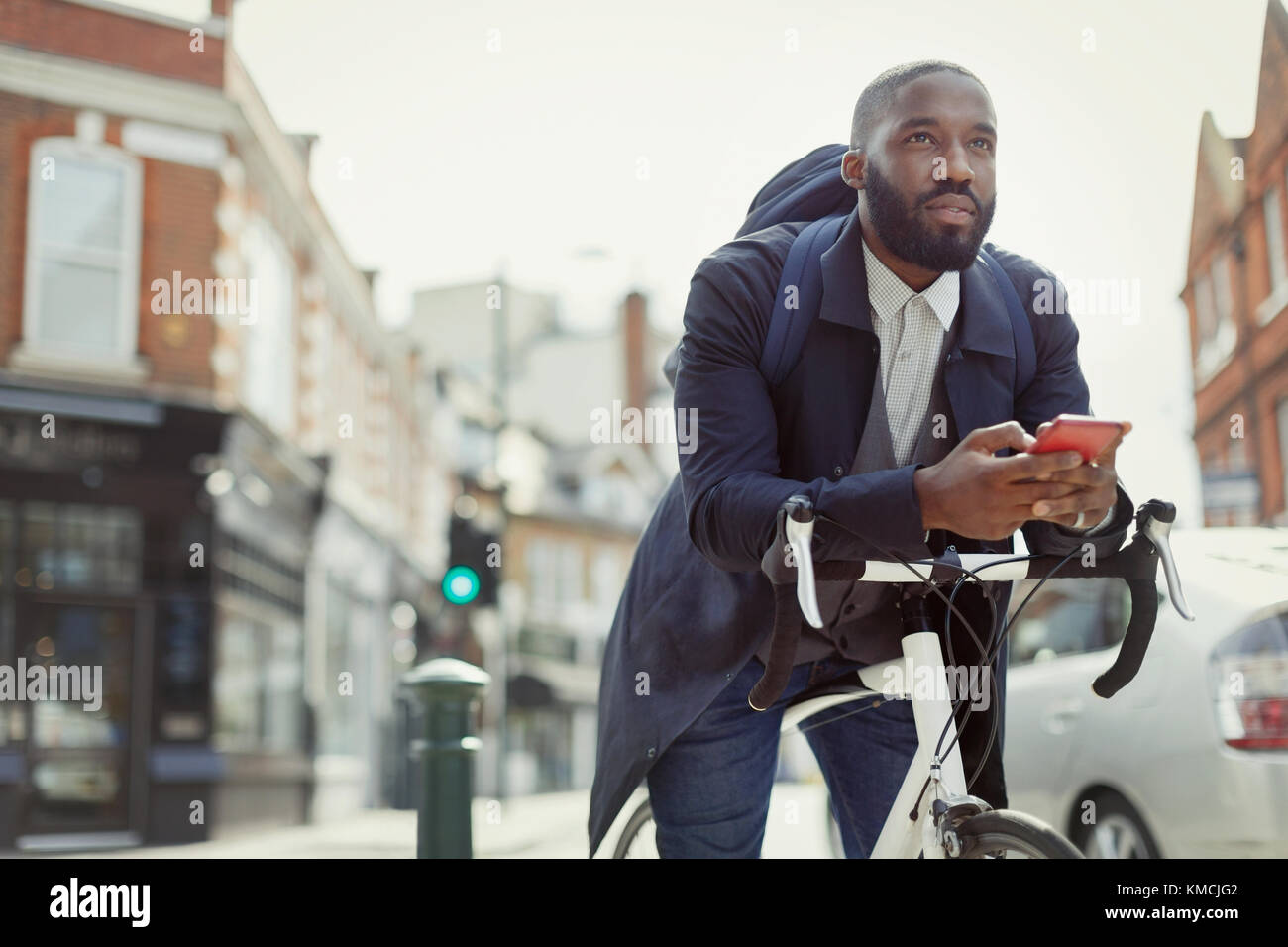 Pensive young businessman texting with cell phone, commuting with bicycle on urban street Stock Photo