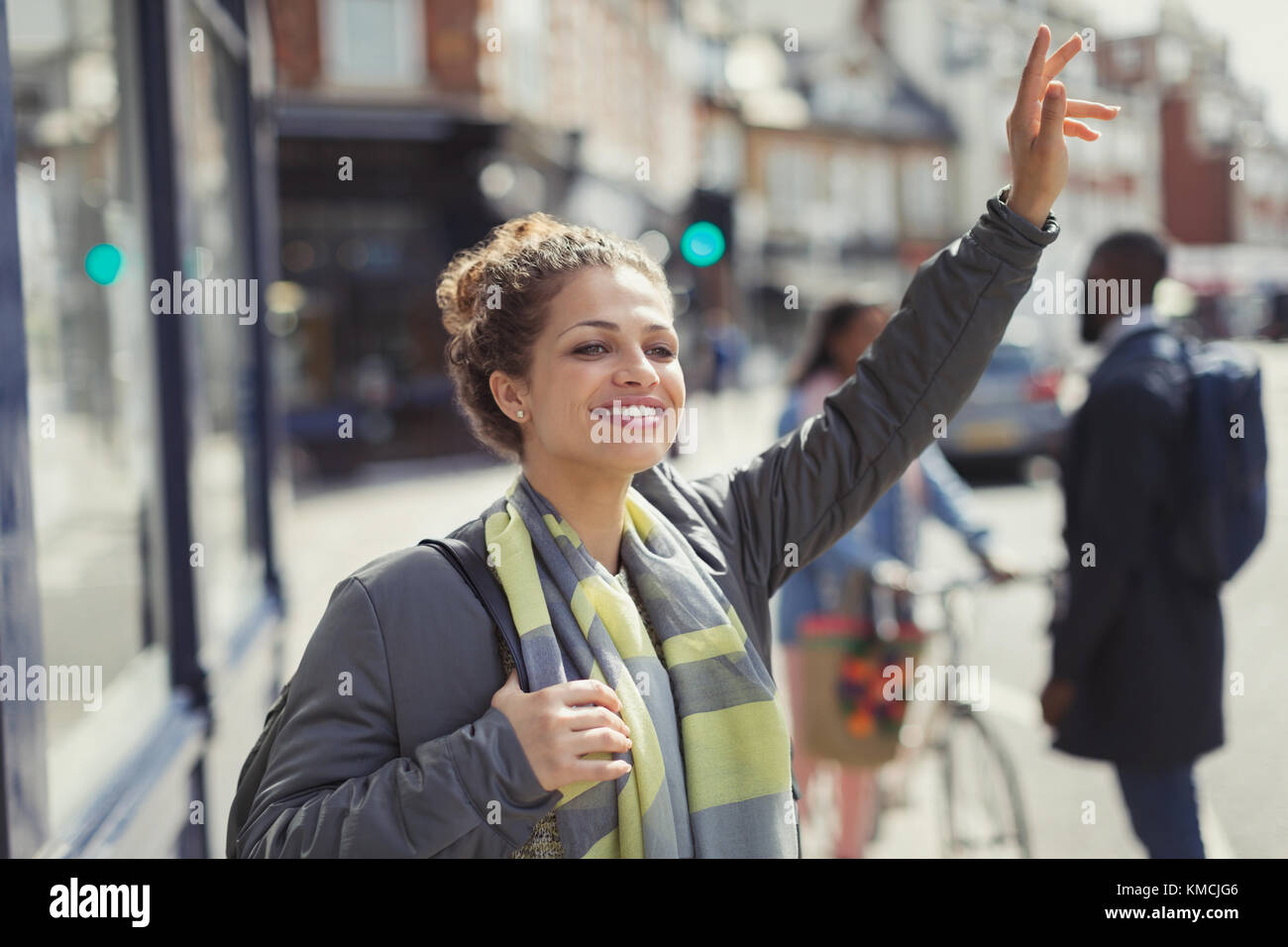 Smiling young woman hailing taxi on sunny urban street Stock Photo