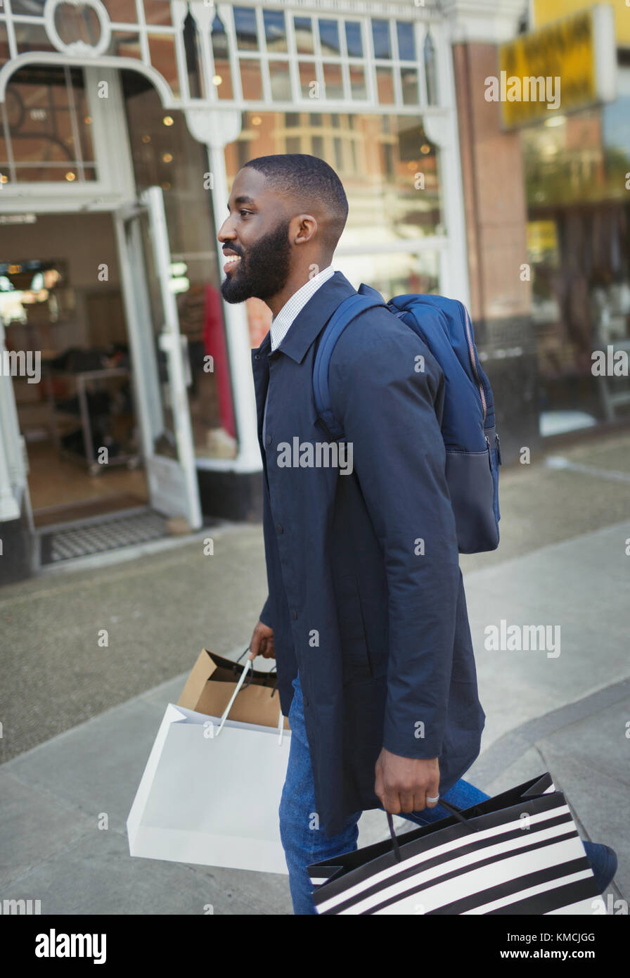 Smiling young man walking along storefront, carrying shopping bags Stock Photo