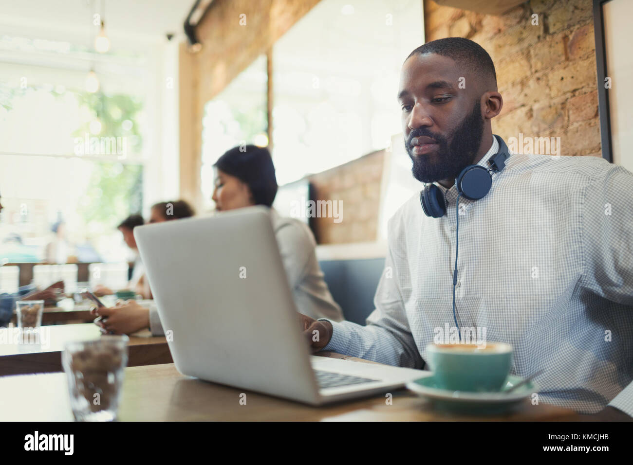 Young man with headphones using laptop and drinking coffee in cafe Stock Photo