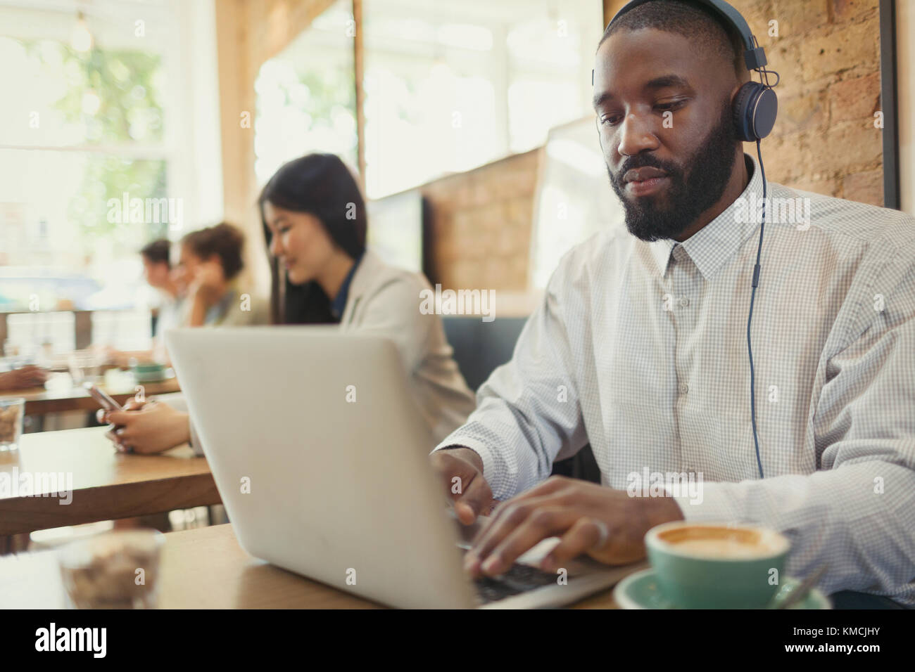 Young man with headphones using laptop and drinking coffee at cafe table Stock Photo