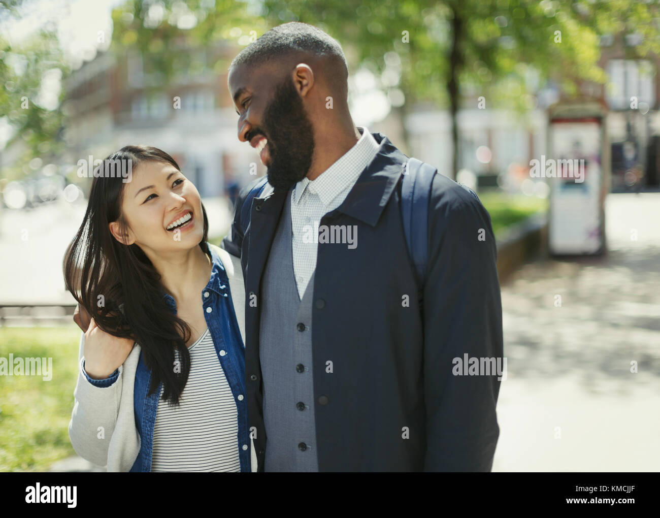 Affectionate couple laughing in sunny urban park Stock Photo