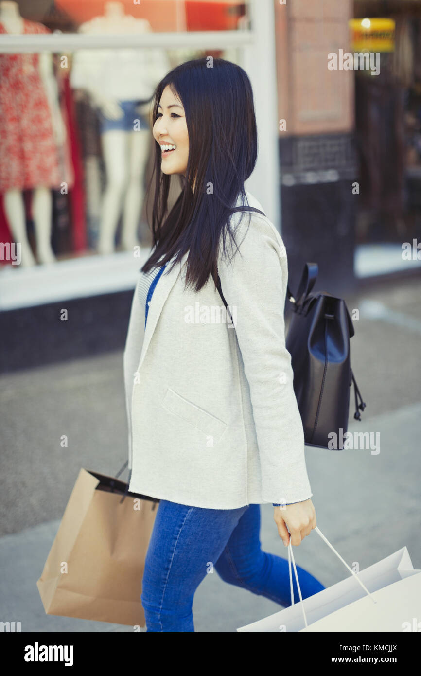 Smiling young woman walking along storefront with shopping bags Stock Photo