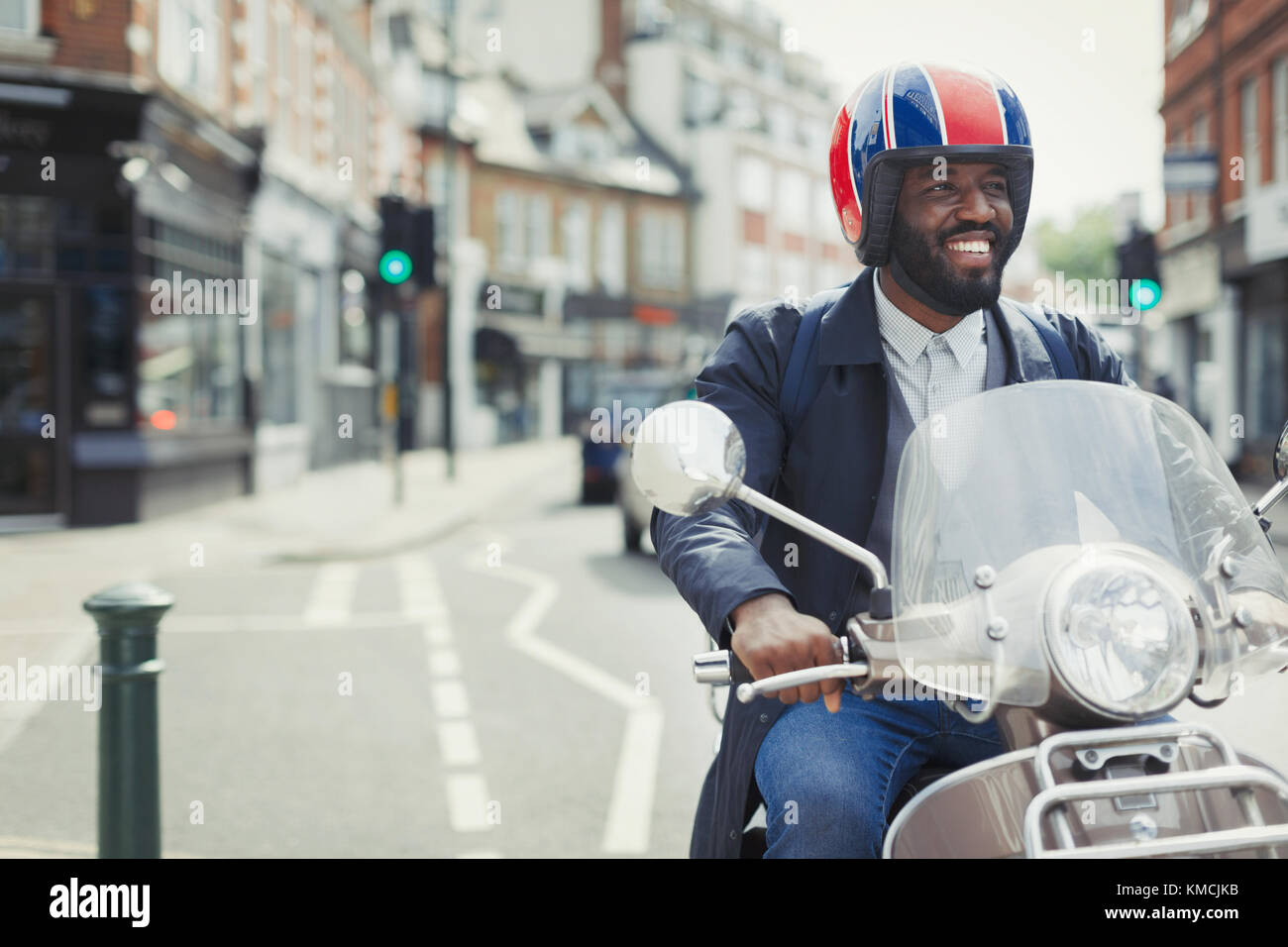 Smiling young businessman in helmet riding motor scooter on urban street Stock Photo