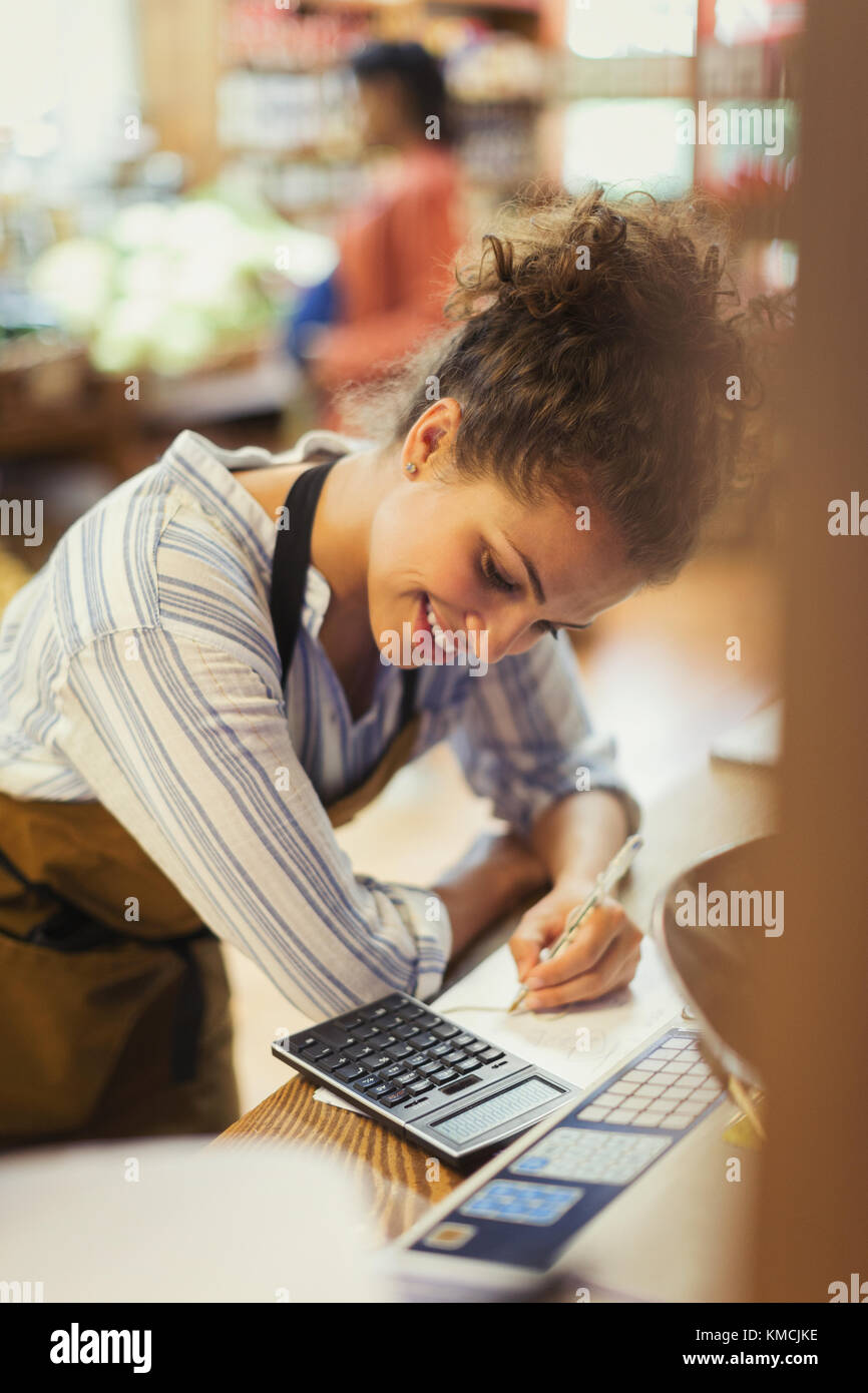 Smiling female cashier using calculator at store counter Stock Photo