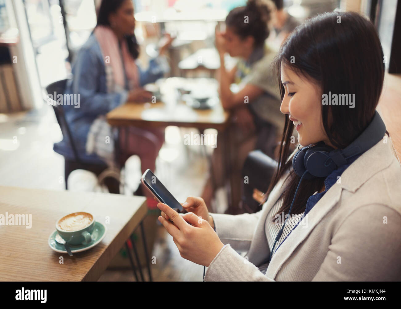 Smiling young woman texting with cell phone and drinking coffee at cafe table Stock Photo