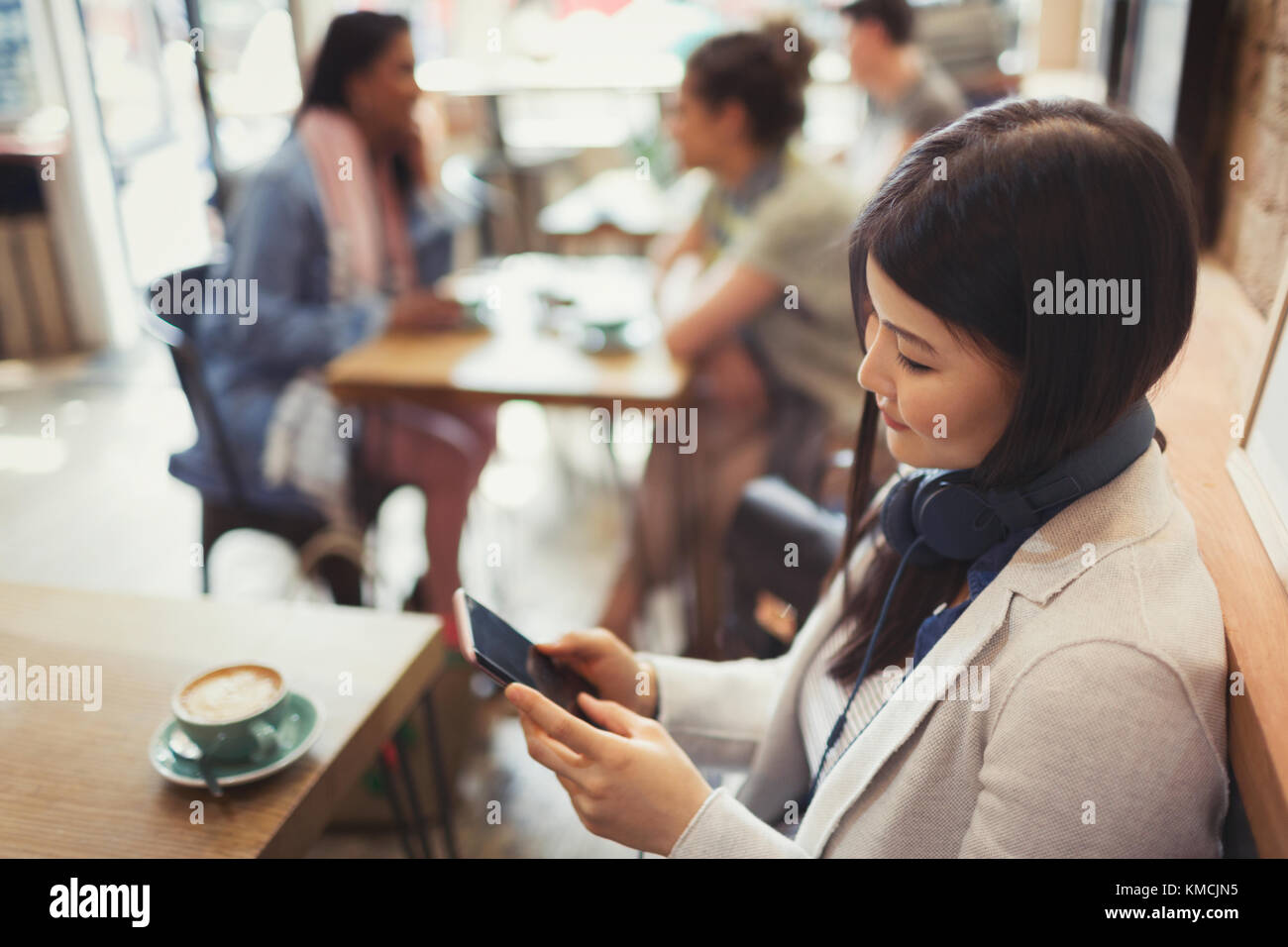 Young woman with headphones texting with cell phone and drinking coffee at cafe table Stock Photo