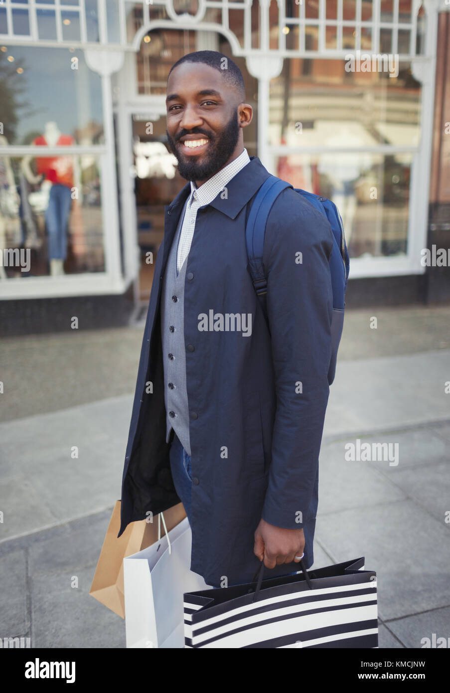 Portrait smiling, confident young man with shopping bags outside storefront Stock Photo