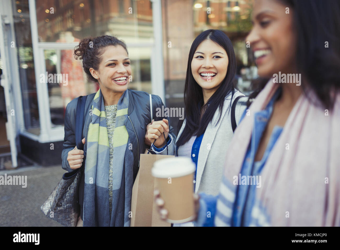 Smiling women friends with shopping bags and coffee outside storefront Stock Photo