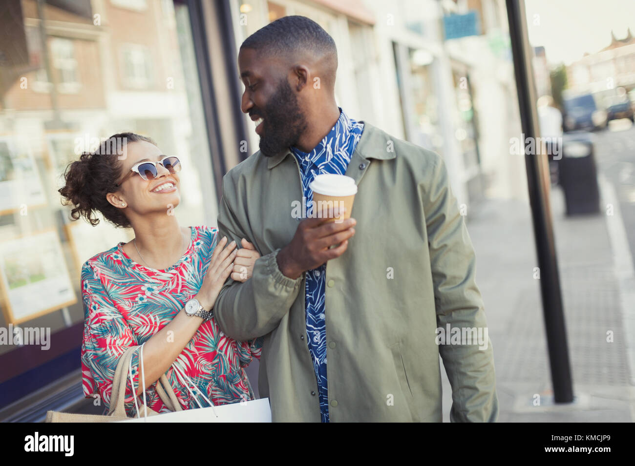 Smiling young couple with coffee walking arm in arm along storefronts Stock Photo