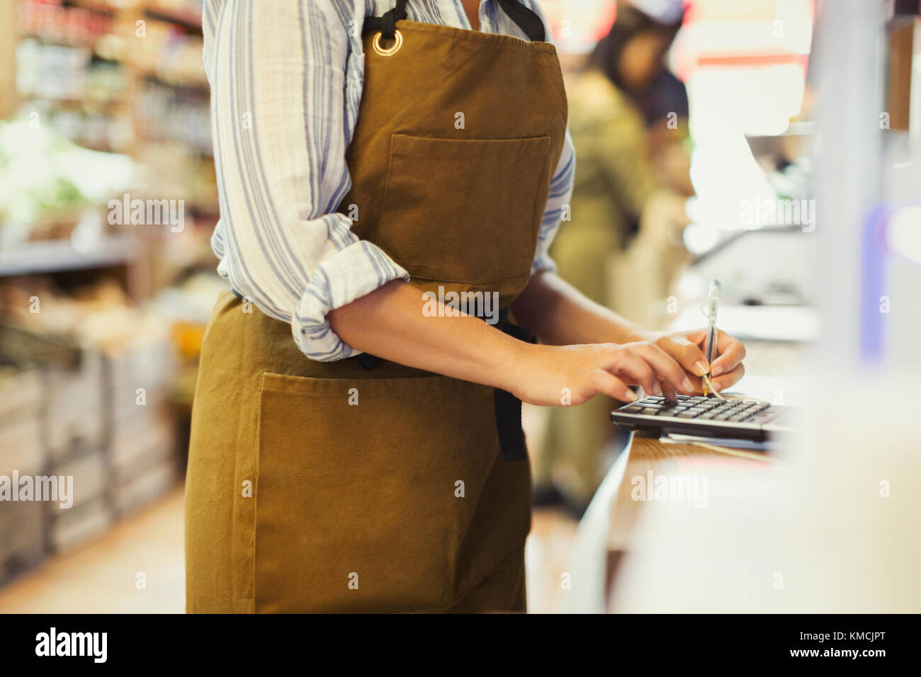 Female cashier using calculator in grocery store Stock Photo