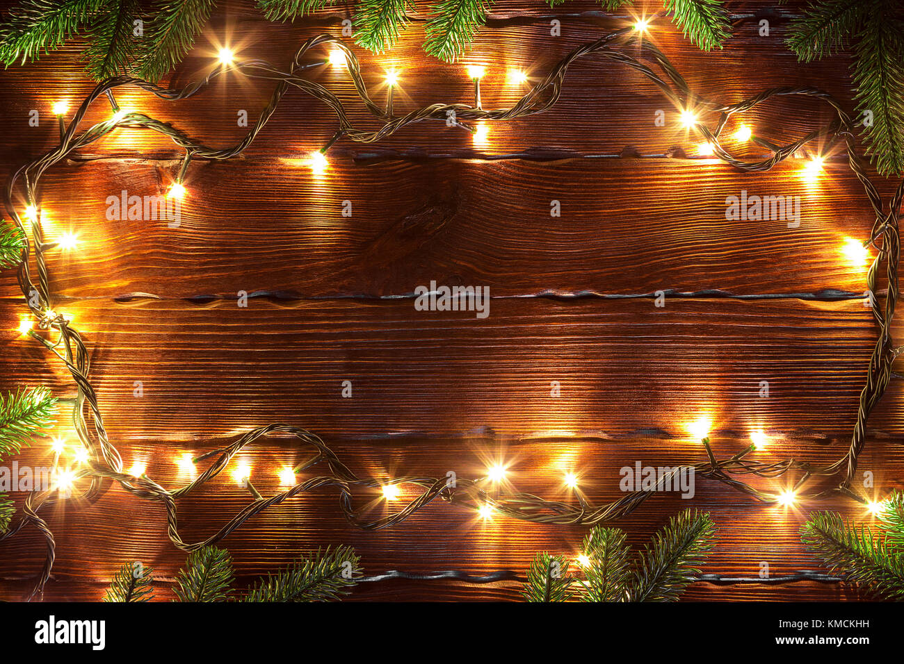 Christmas bokeh background. Glowing golden garland on a brown wooden table with branches of Christmas tree. Stock Photo