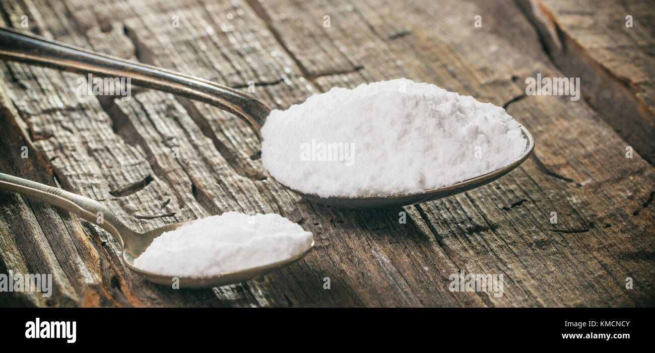Tablespoon and teaspoon with baking soda, on wooden surface. Close up
