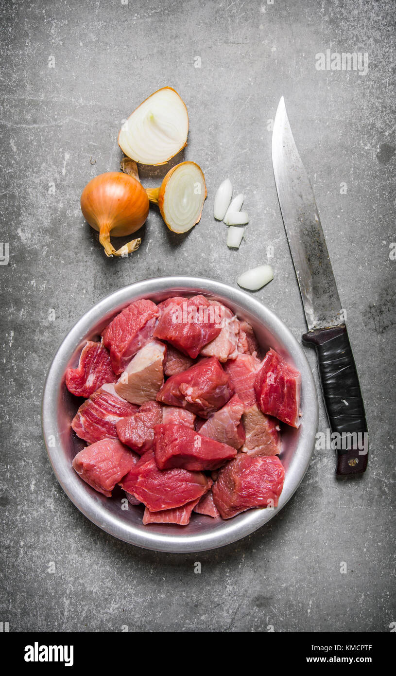 https://c8.alamy.com/comp/KMCPTF/pieces-of-raw-meat-in-a-bowl-with-a-chopping-knife-and-a-onion-on-KMCPTF.jpg