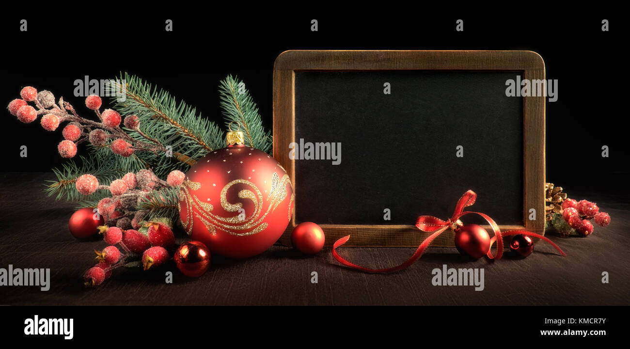 Blackboard with text space surrounded by Christmas decorations on black background. Panoramic framing for banner or web design. Toned image. Top part  Stock Photo