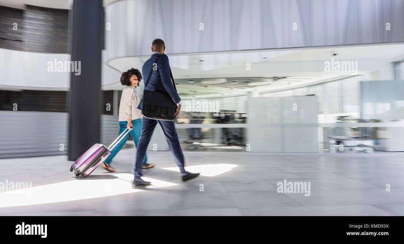 Businessman and businesswoman walking,pulling suitcase in modern office lobby Stock Photo