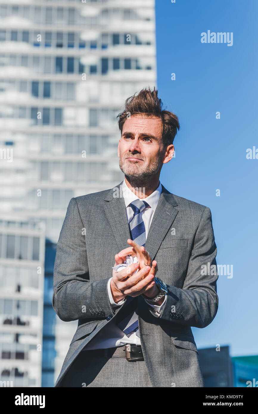 angry businessman stands in front of a skyscraper and crumples up documents Stock Photo