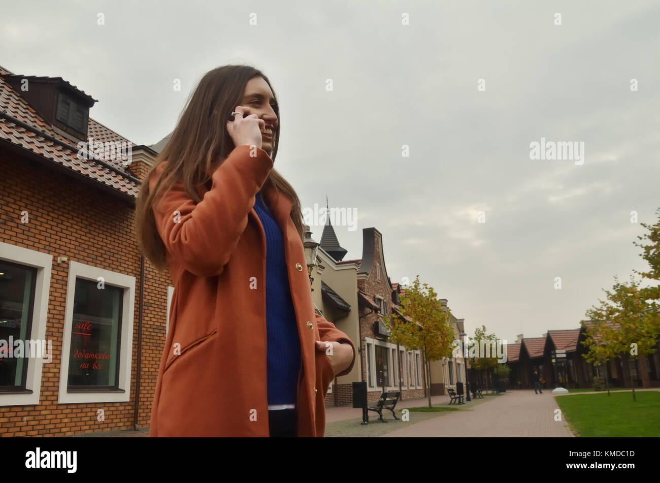 A young girl speaks on the phone, standing in the middle of the alley, looking from below and from the side. Smiling face, looking forward, around the Stock Photo