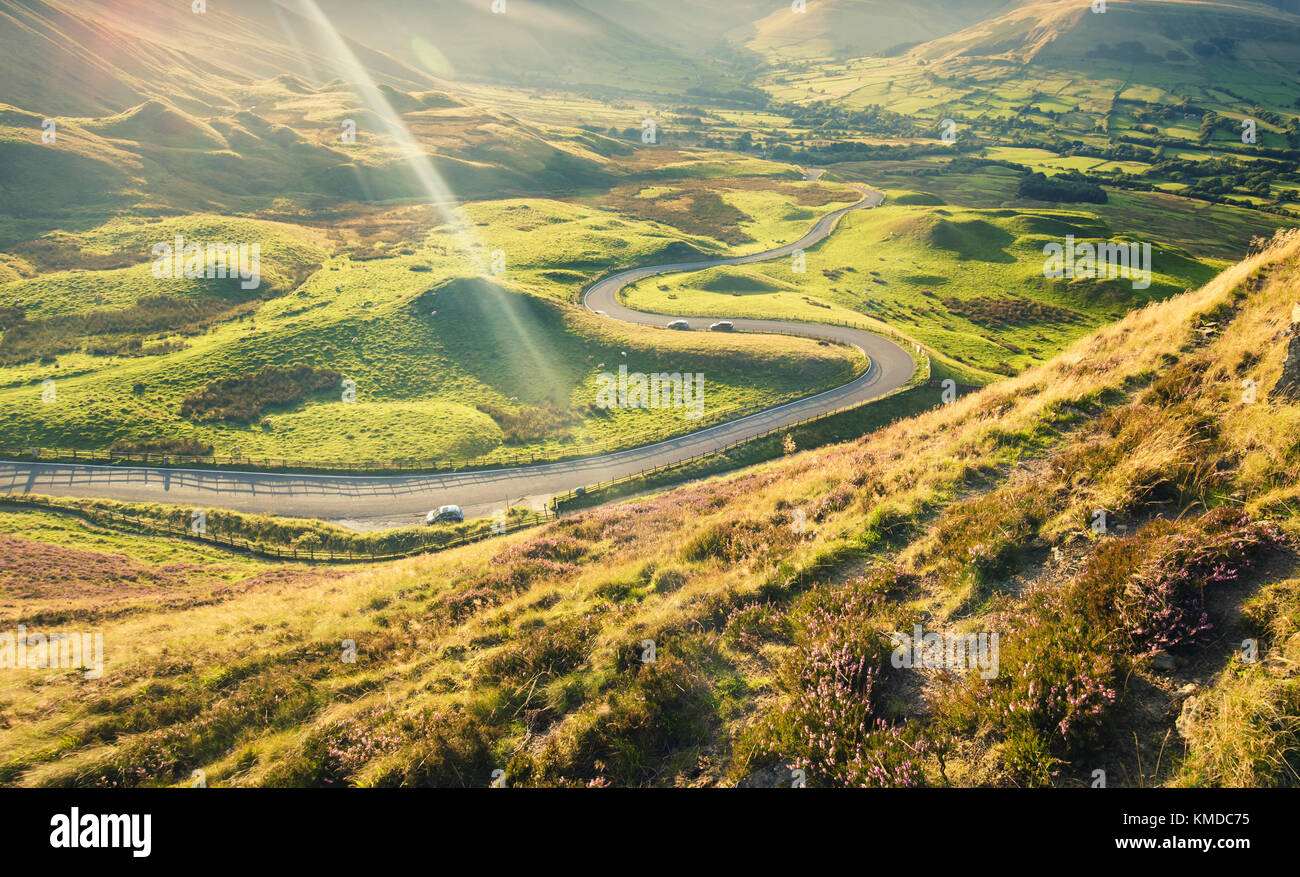 Scenic serpentine road in warm sunset light at summer. Elevated view from slopes in heather of Mam Tor Stock Photo