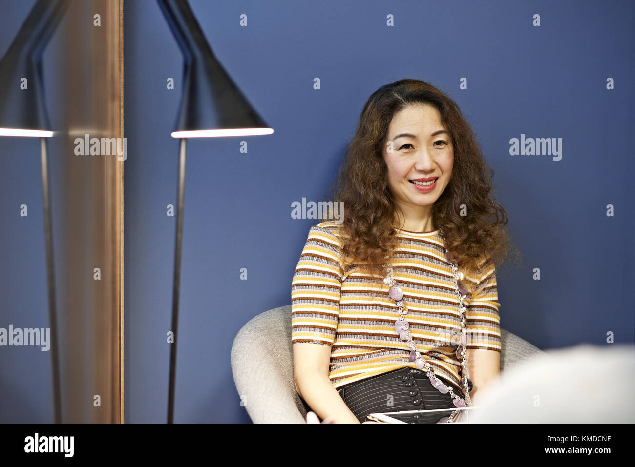 Asian businesswoman in a contemporary office smiling at a colleague off-camera Stock Photo